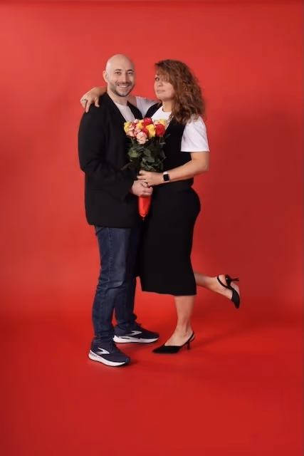 Leonid and Olga, the family founders of HQ Portraits, smiling together on a red studio backdrop