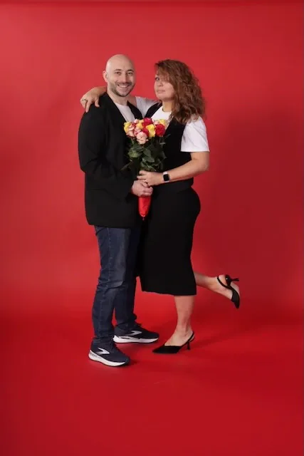 Leonid and Olga, the family founders of HQ Portraits, smiling together on a red studio backdrop